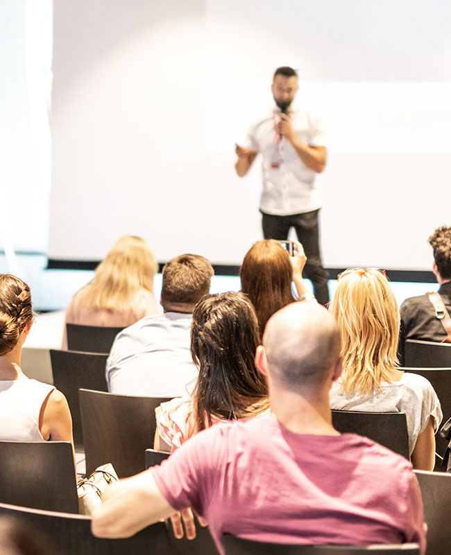 Image of a male speaker with a microphone in front of an audience